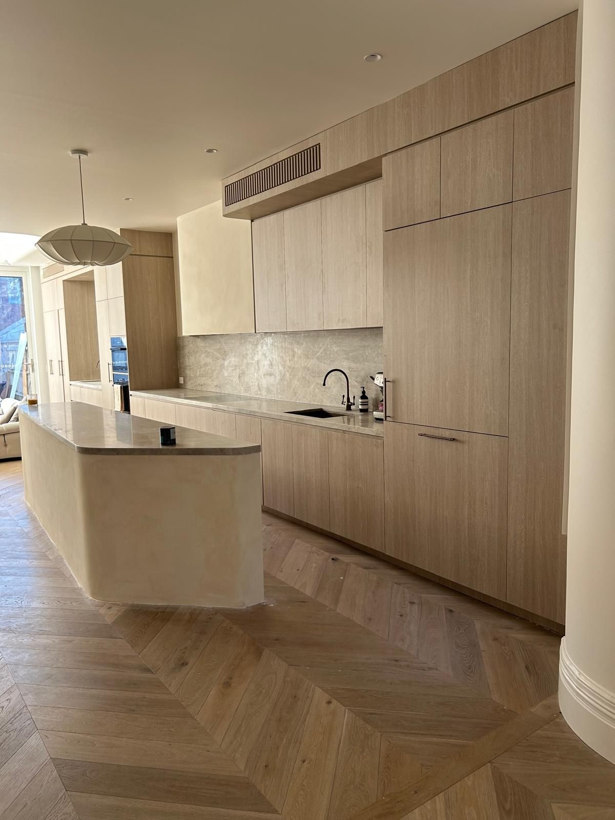 Pale oak kitchen joinery with a stone-topped island and a chevron oak floor in a completed residence, inner Melbourne.