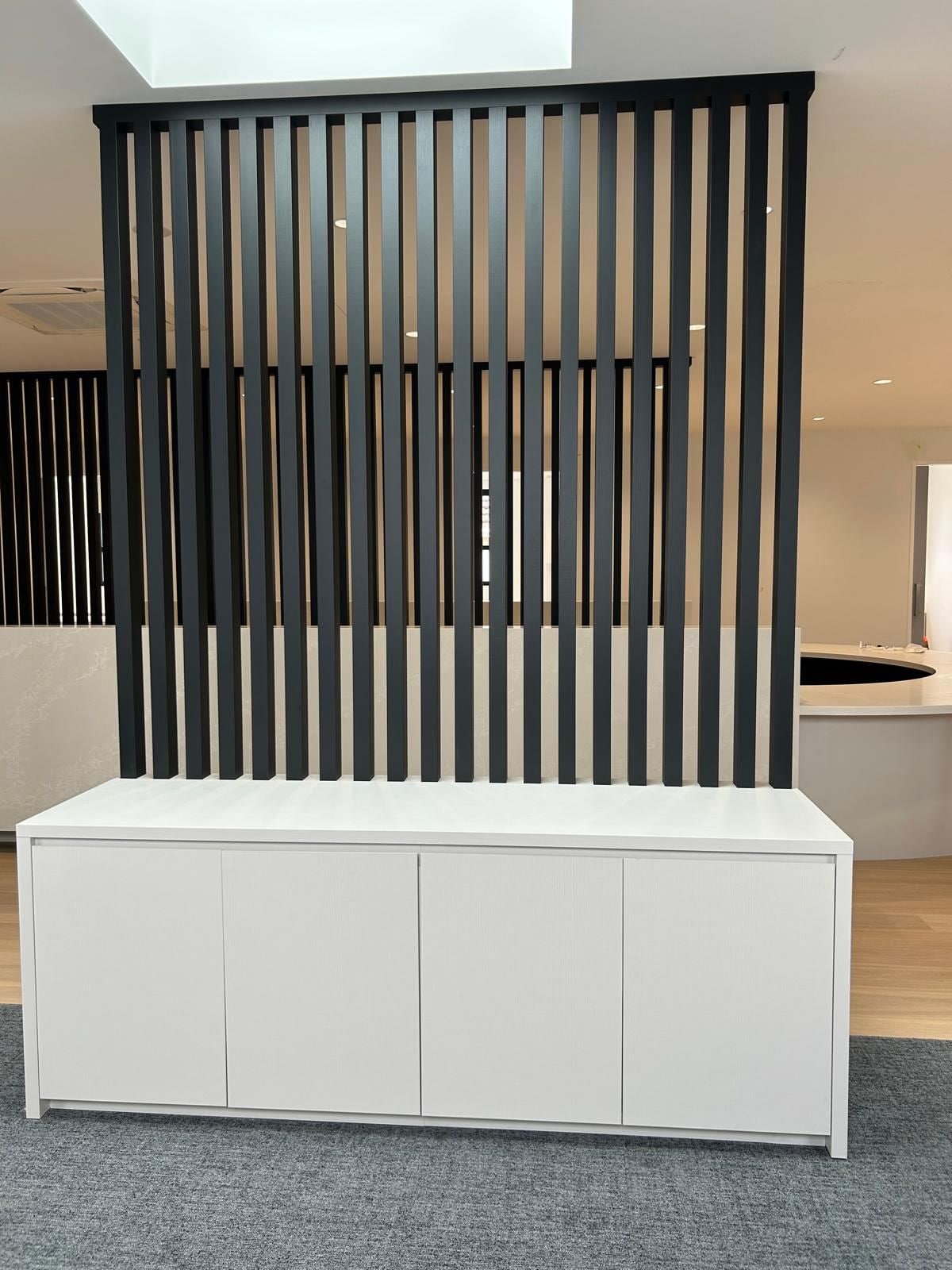 Black vertical slat screen running from the ceiling to a white four-door cabinet, with a curved stone-look counter beyond, Bayside.