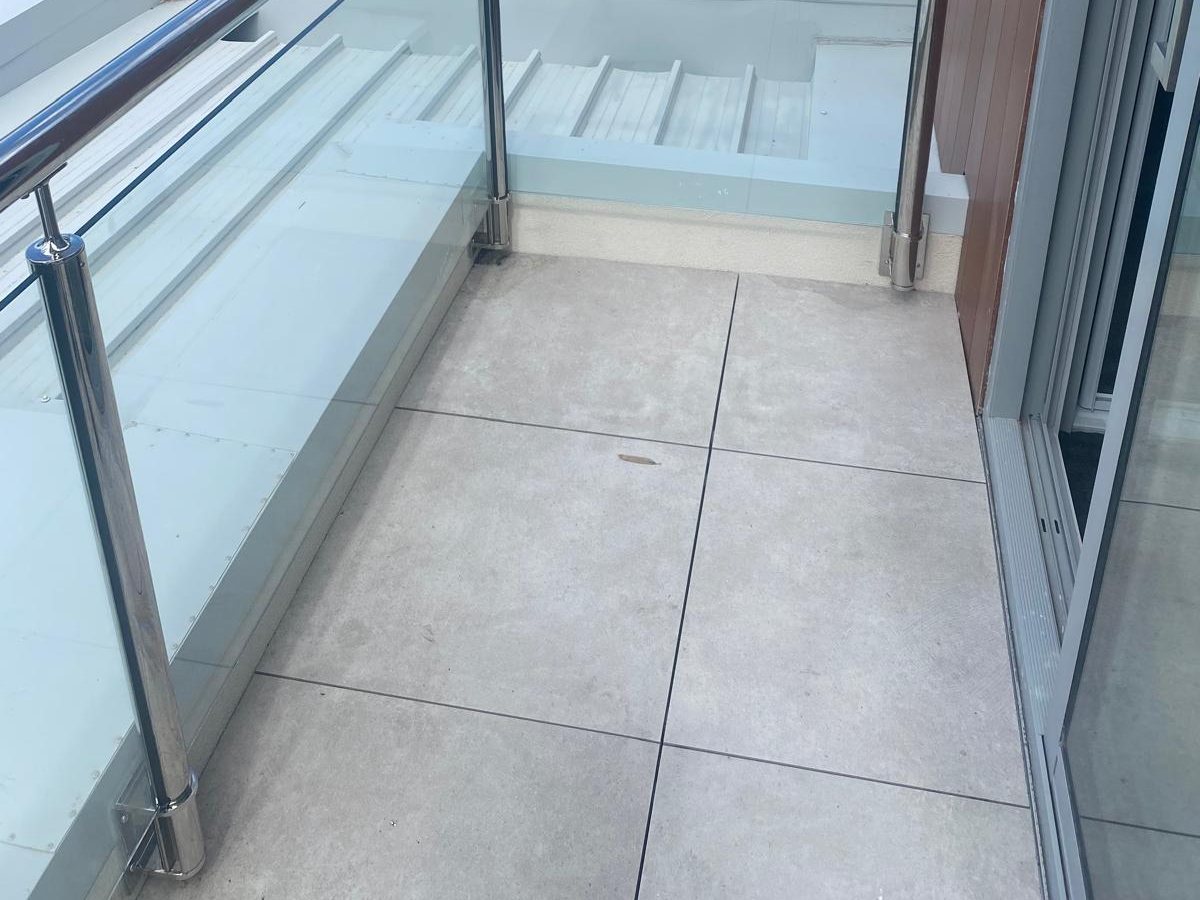 The finished balcony seen from the doorway, with new large-format tiles and a frameless glass balustrade on stainless posts, Mornington Peninsula.