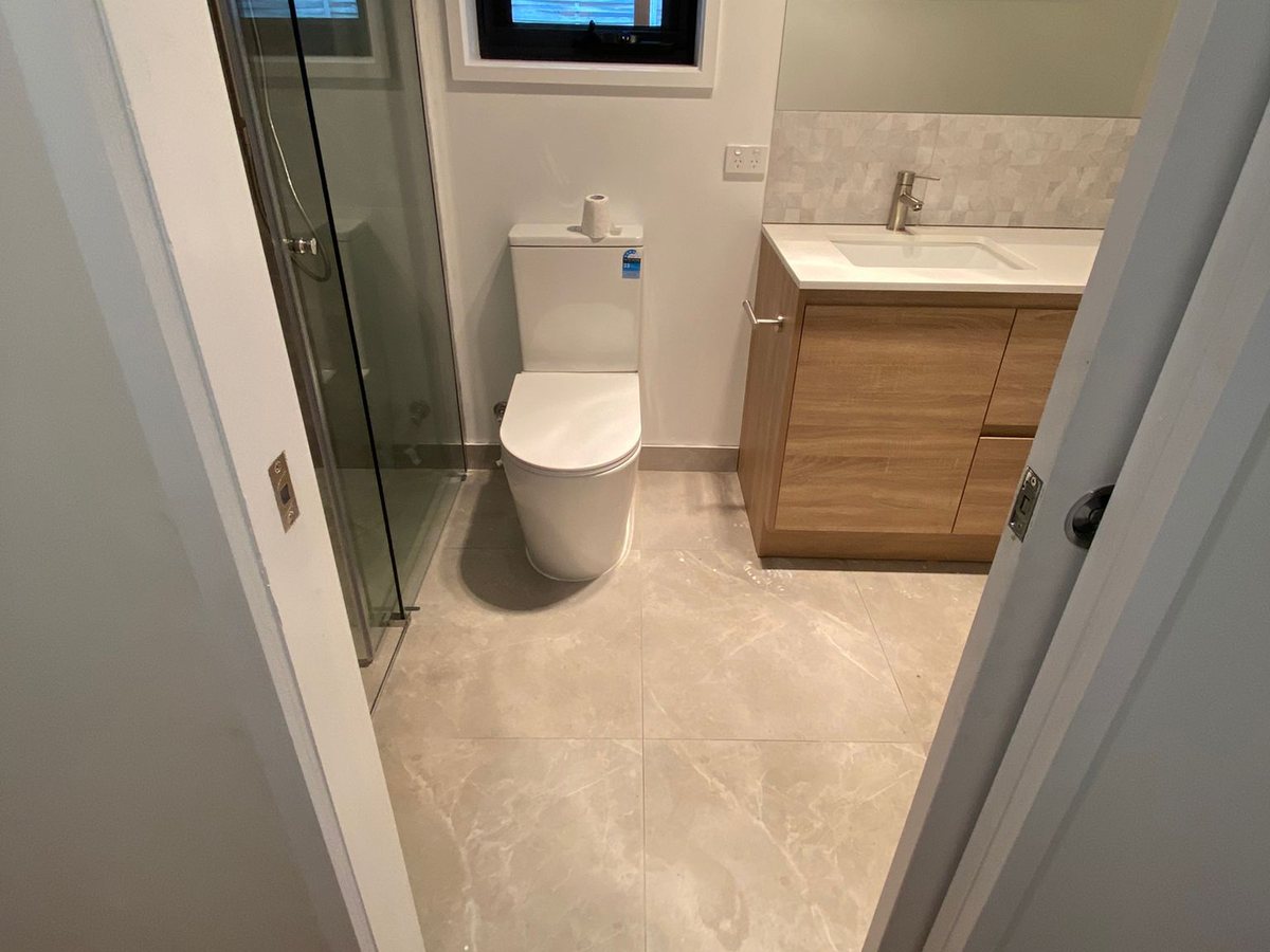 A finished ensuite with a frameless glass shower screen, a timber-look vanity with a stone top and large-format stone-look floor tiles, Melbourne’s south-east.