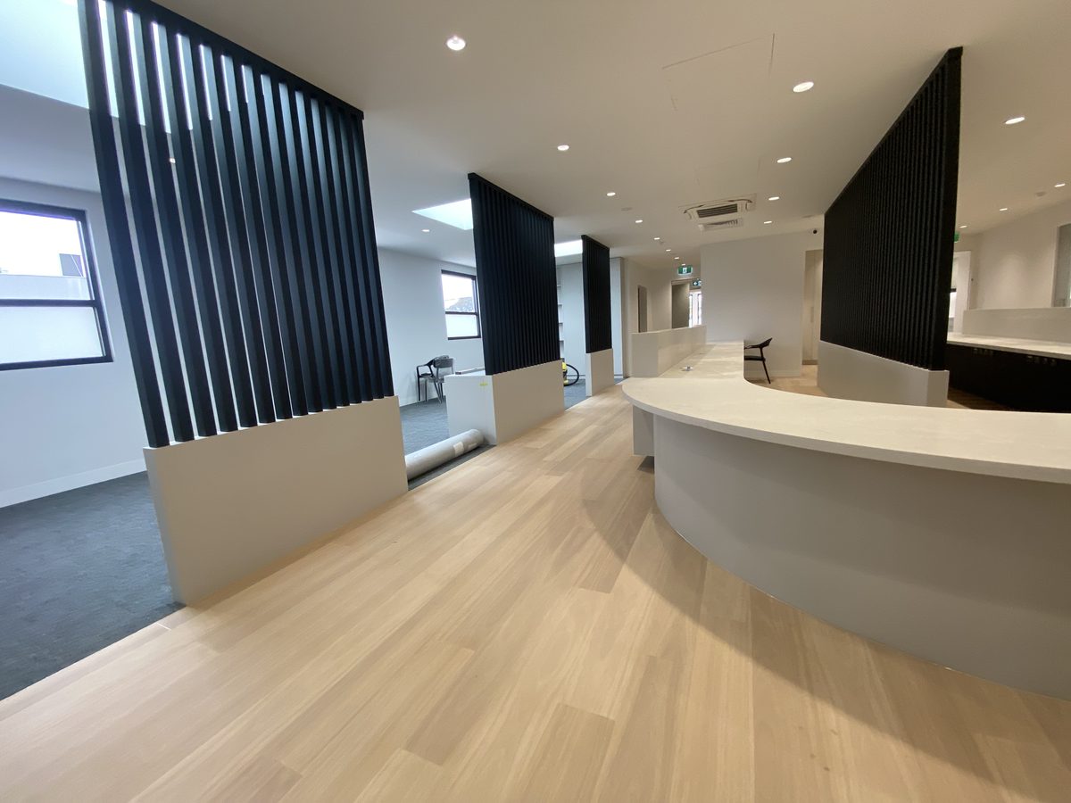 Reception with black slatted timber screens on low plinths and a curved counter, at handover, Bayside.