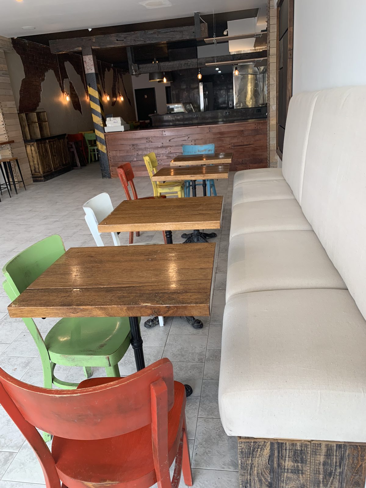 Restaurant dining room with timber tables and painted chairs beside an upholstered banquette, looking to the recycled hardwood counter, Coal Workshop, Melbourne’s west.
