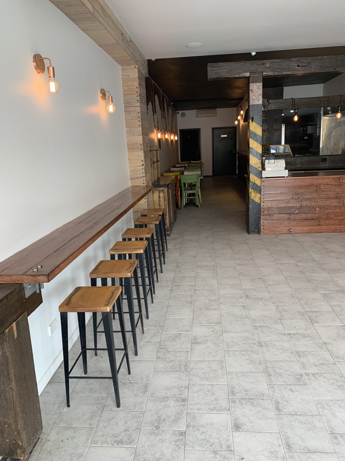 Narrow restaurant looking to the back, a recycled timber wall bench with stools on one side and the recycled hardwood service counter on the other, Coal Workshop, Melbourne’s west.
