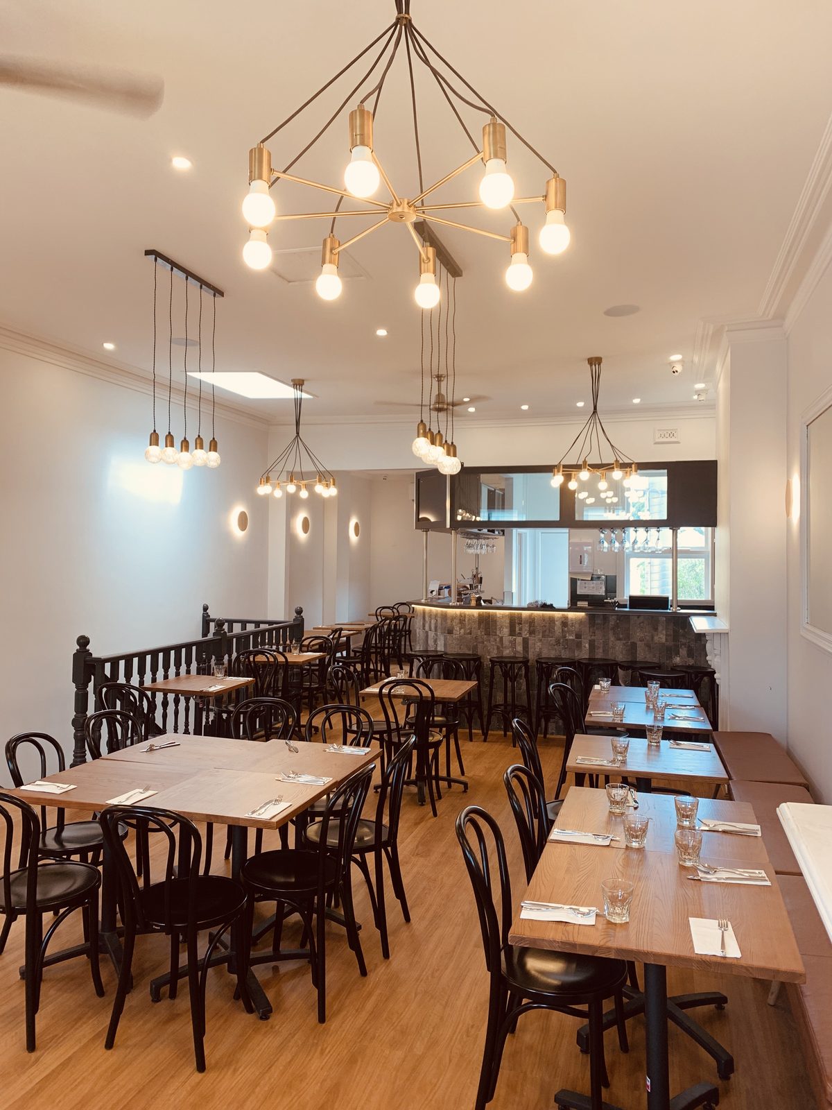 Upstairs restaurant dining room set for service, with timber tables, bentwood chairs, brass pendant lights and a tiled bar at the far end, inner Melbourne.