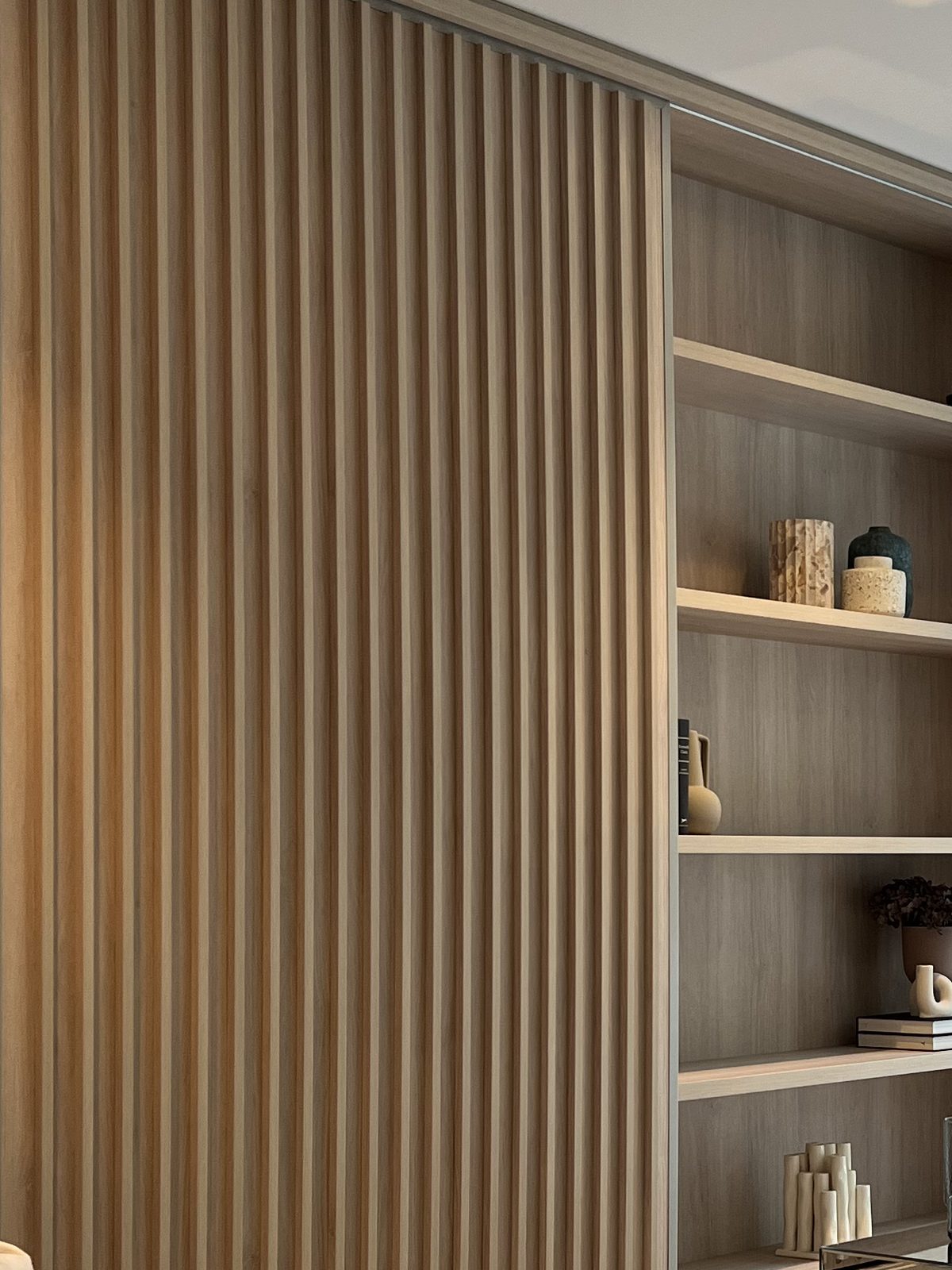 Vertical oak batten panel beside built-in open shelving in a finished apartment, Bayside.