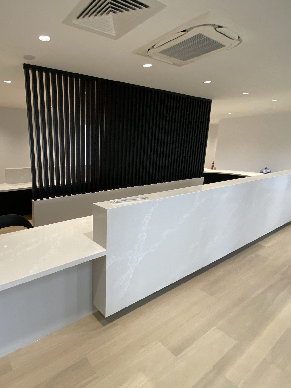 Medical centre reception counter in veined stone with a black timber batten screen behind, Bayside.