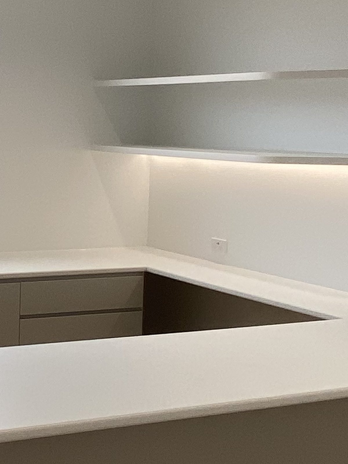 Floating shelves with strip lighting above a stone benchtop return in a consulting room, Bayside.