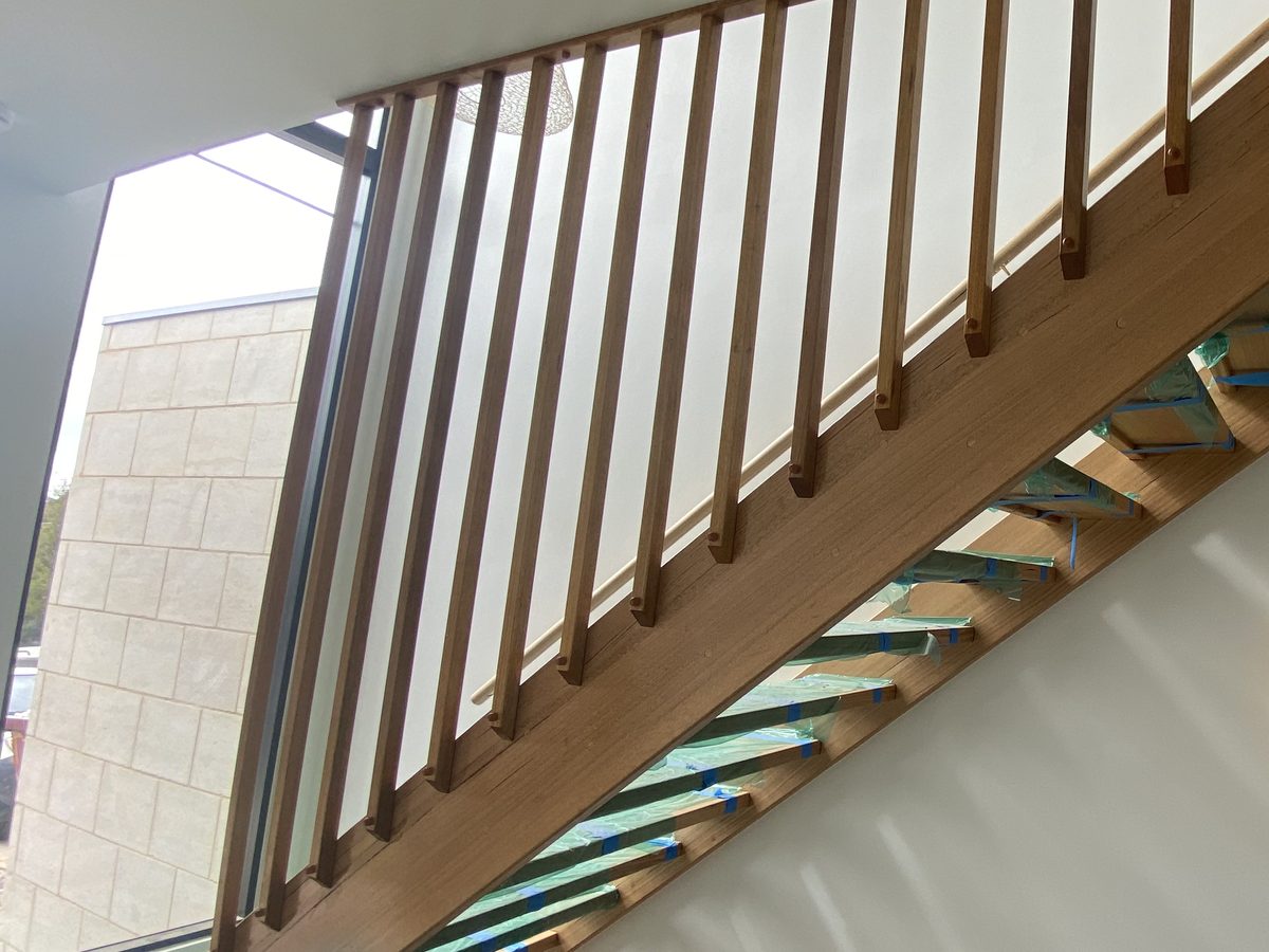 Timber staircase seen from below, its treads wrapped in green protective film held with blue tape, Mornington Peninsula.
