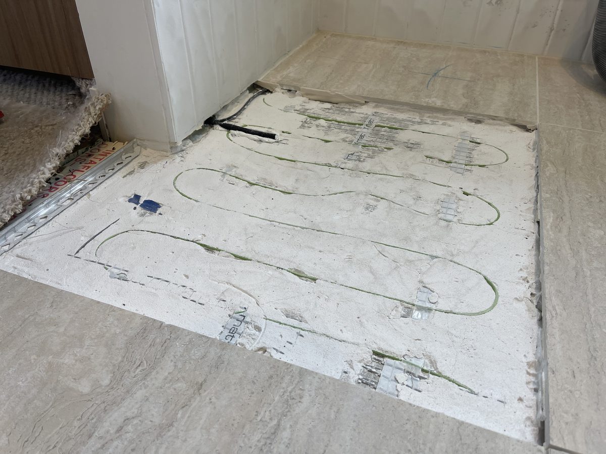 Tiled floor with a section of tiles lifted to expose the in-floor heating cable in the adhesive bed, Mornington Peninsula.