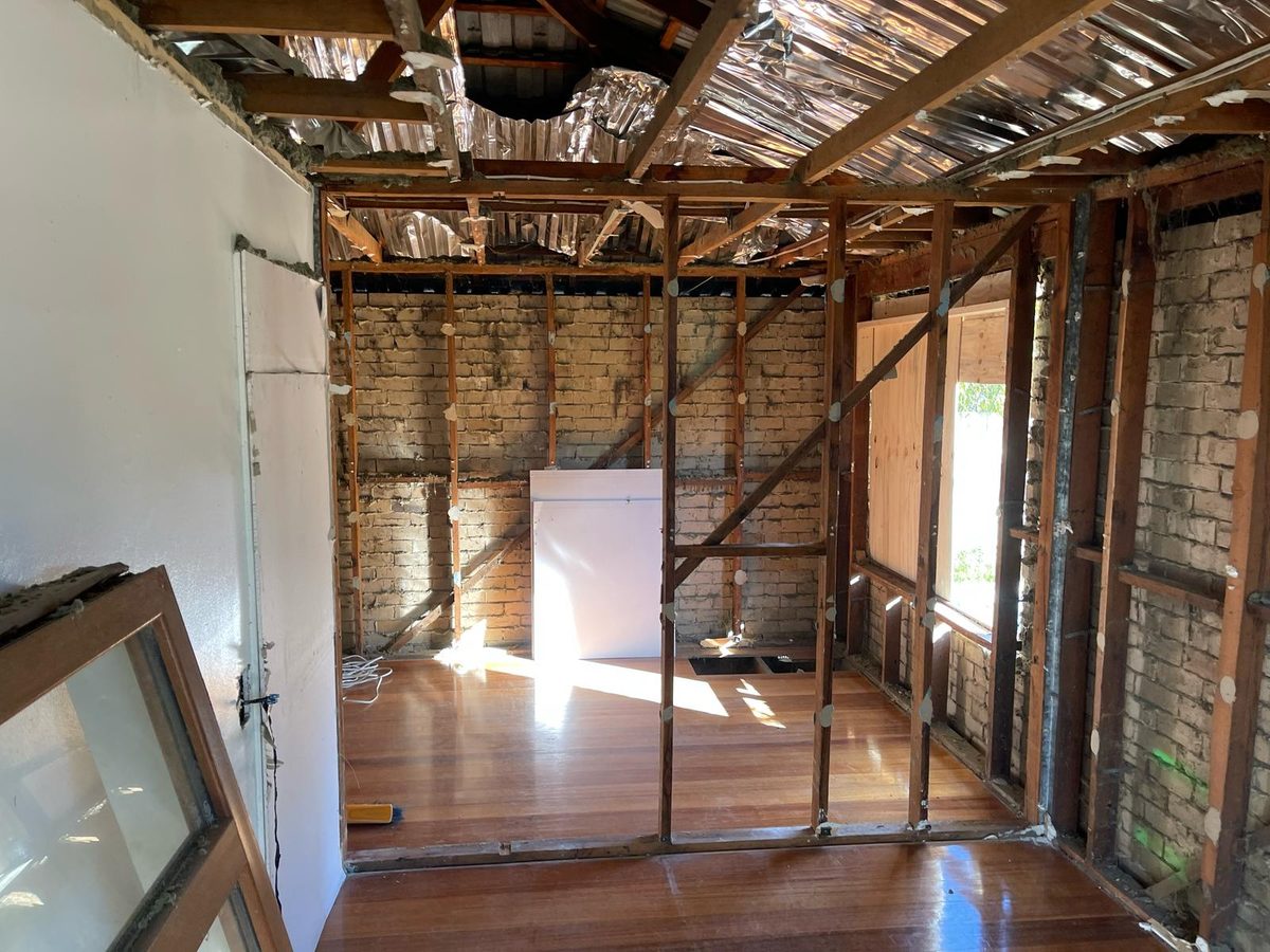 A room stripped back to structure, plaster removed to the internal brickwork, timber studs and diagonal bracing exposed and the ceiling opened to the rafters, Melbourne’s south-east.