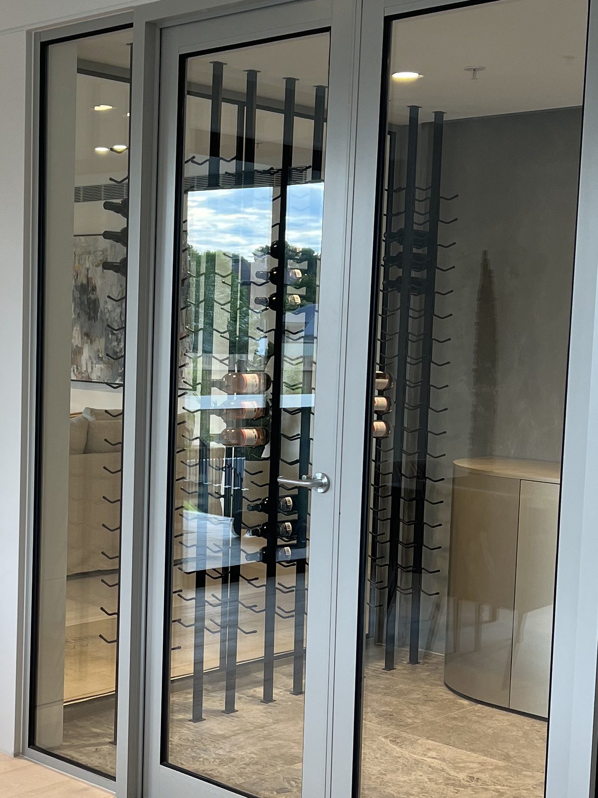 Glazed wine storage enclosure with a powder-coated frame and black steel racking, in a finished apartment, Bayside.