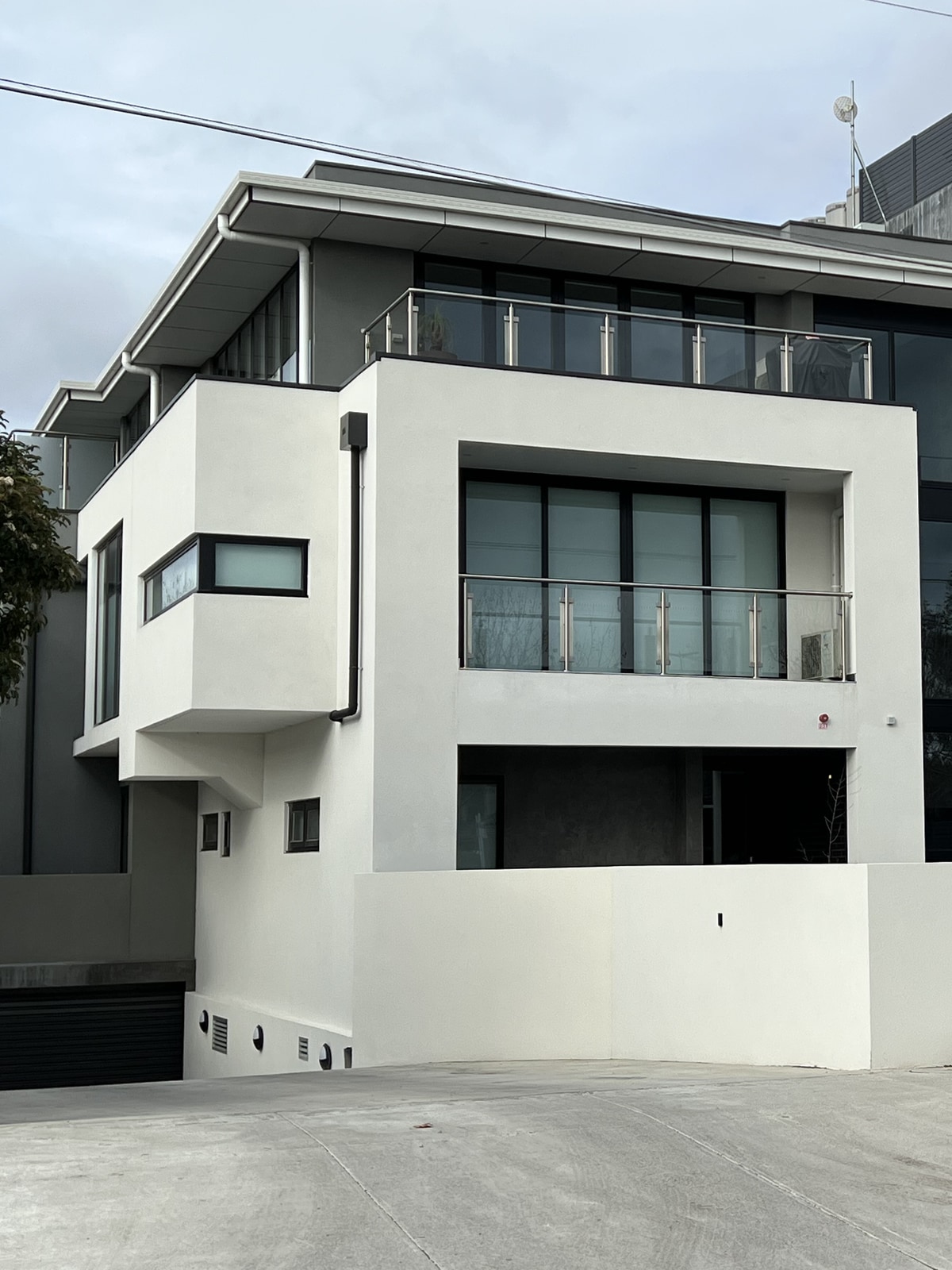 Street view of a finished rendered multi-residential building with stacked glass balustrade balconies and a recessed ground floor entry, Melbourne’s inner north-west.