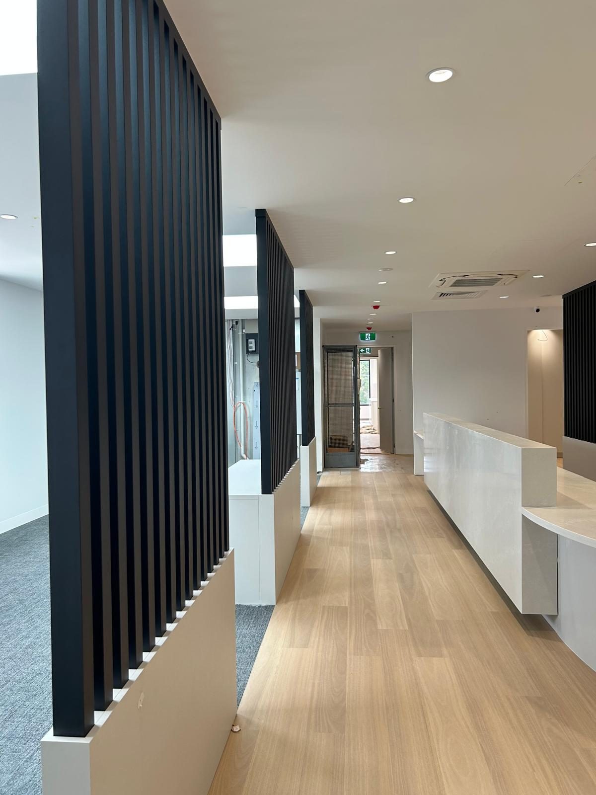 Completed commercial fitout corridor with a black slatted screen wall, solid surface reception counter and timber floor, Brighton East.